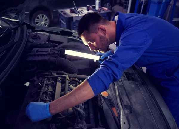 Mechanic man with lamp repairing car at workshop — Stock Photo, Image