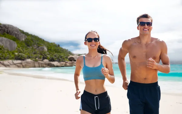 Casal em roupas esportivas correndo ao longo da praia — Fotografia de Stock