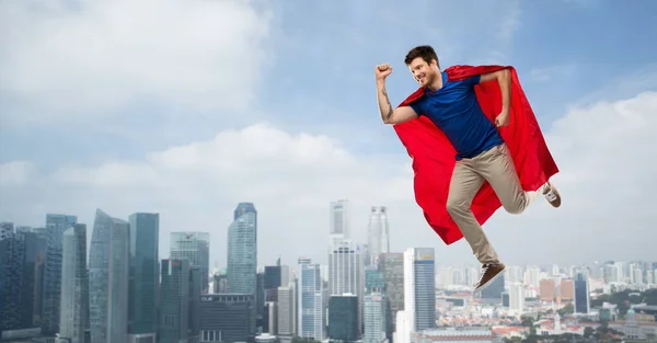 Man in red superhero cape flying in air over city — Stock Photo, Image