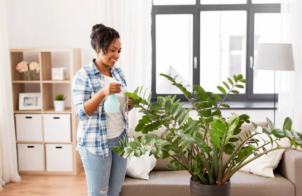Heureuse femme africaine pulvérisation plantes d'intérieur à la maison — Photo