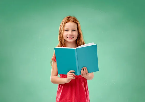 Menina estudante vermelho com livro sobre placa de giz escola — Fotografia de Stock