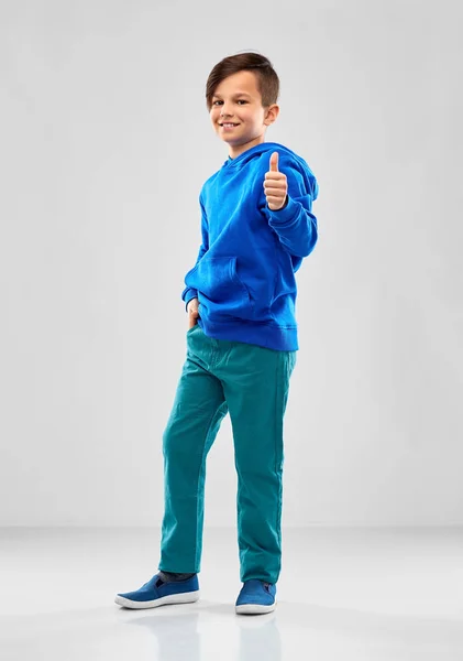 Sorrindo menino com capuz azul mostrando os polegares para cima — Fotografia de Stock