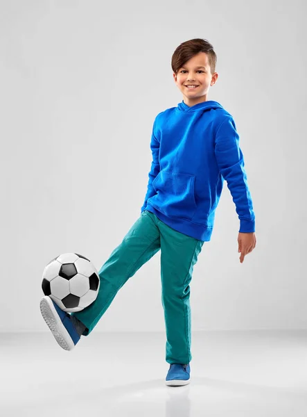Улыбающийся мальчик в синей толстовке играет в футбол — стоковое фото