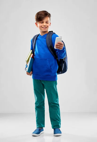 Hallgató fiú okostelefonnal, könyvekkel és iskolazsák — Stock Fotó