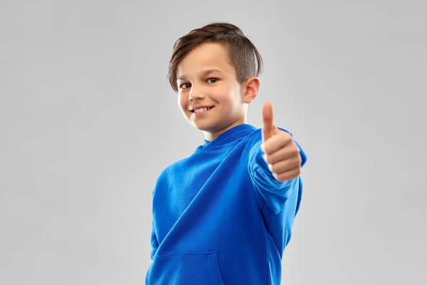 Sorrindo menino com capuz azul mostrando os polegares para cima — Fotografia de Stock