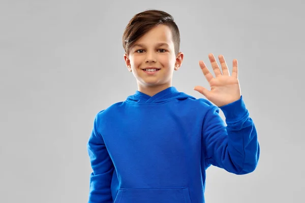 Χαμογελαστός αγόρι με μπλε κουκούλα κουνώντας το χέρι — Φωτογραφία Αρχείου