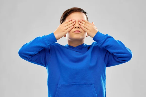 Pojke i blå hoodie stänga ögonen med händerna — Stockfoto