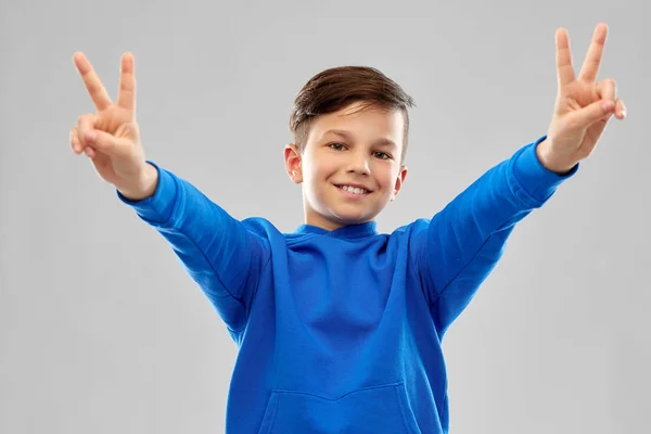 Menino sorridente com capuz azul mostrando gesto de paz — Fotografia de Stock