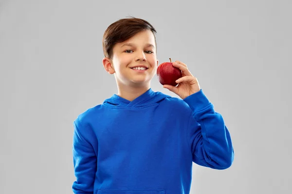 Mosolyogva fiú kék kapucnis pulcsit vörös almával — Stock Fotó