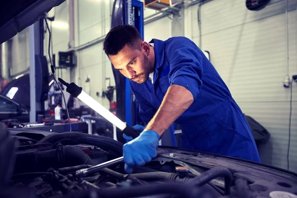 Mecânico homem com lâmpada reparando carro na oficina — Fotografia de Stock