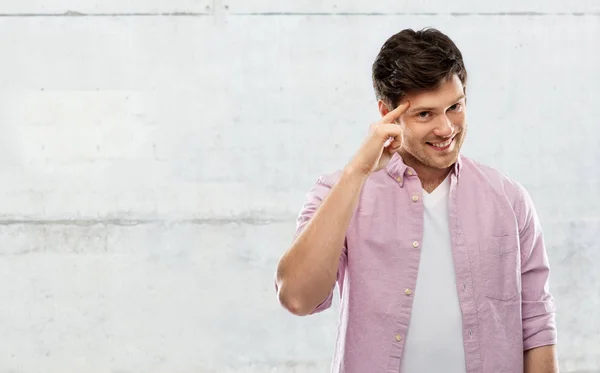 Smiling young man pointing finger to his head — Stock Photo, Image