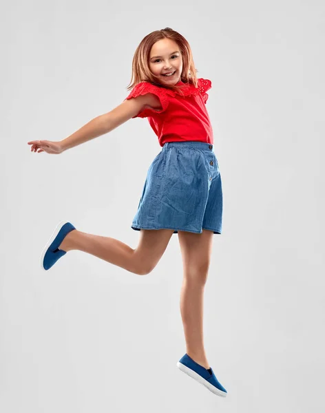 Gelukkig glimlachend meisje in rood shirt en rok springen — Stockfoto