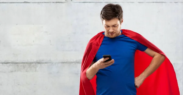 Młody człowiek w Przylądek czerwony superbohatera za pomocą smartfona — Zdjęcie stockowe
