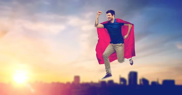 Hombre en capa de superhéroe volando sobre el atardecer en la ciudad — Foto de Stock