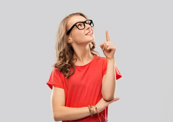 Lächelndes Studentenmädchen mit Brille zeigt mit dem Finger nach oben — Stockfoto