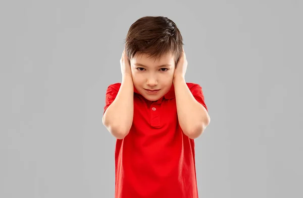 Niño estresado en camiseta roja cerrando las orejas por las manos —  Fotos de Stock