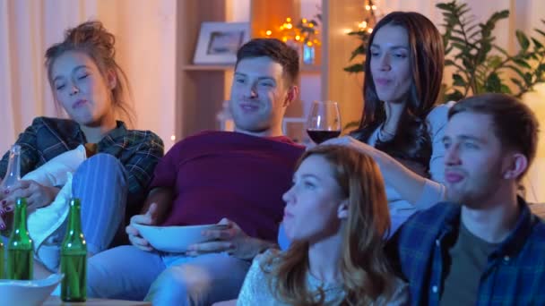 Друзья с напитками и закусками смотрят телевизор дома — стоковое видео
