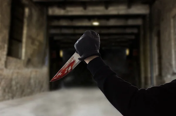 Mano en guante con cuchillo ensangrentado sobre puerta oscura — Foto de Stock