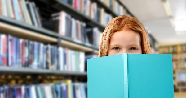 Uśmiechnięte czerwone włosy dziewczyna czytania książki w bibliotece — Zdjęcie stockowe