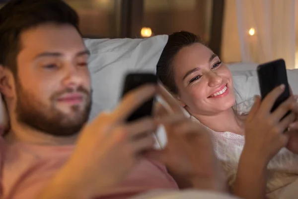 Pareja usando teléfonos inteligentes en la cama por la noche — Foto de Stock