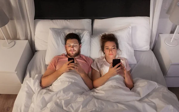 Pár pomocí chytrých telefonů v posteli v noci — Stock fotografie