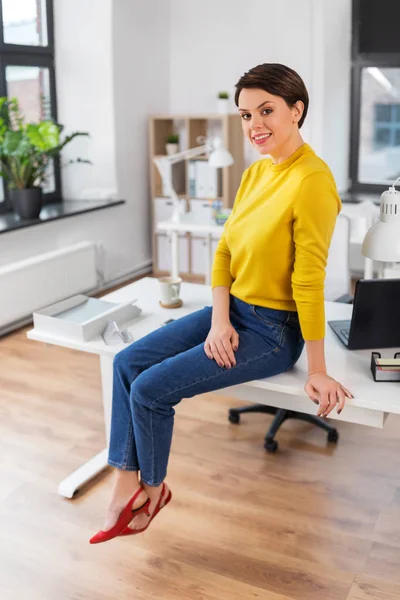 Glückliche Geschäftsfrau sitzt auf Schreibtisch im Büro — Stockfoto