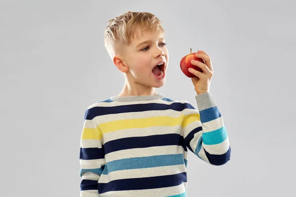 Junge im gestreiften Pullover isst roten Apfel — Stockfoto