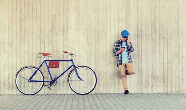 Хипстер человек в наушниках со смартфоном и велосипедом — стоковое фото