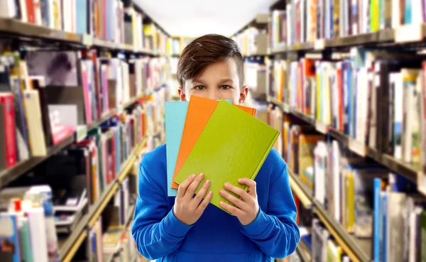 Tímido estudante menino escondido atrás de livros na biblioteca — Fotografia de Stock