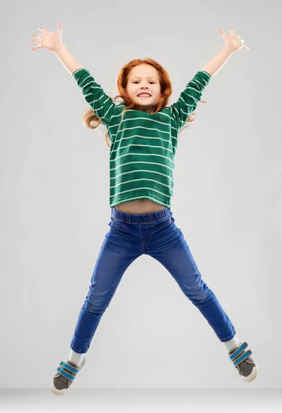 Smiling red haired girl in striped shirt jumping — Stock Photo, Image