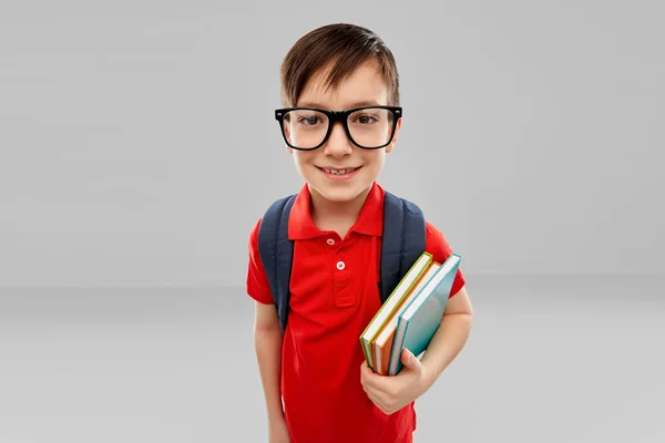 Niño estudiante sonriente en gafas con libros y bolsa — Foto de Stock