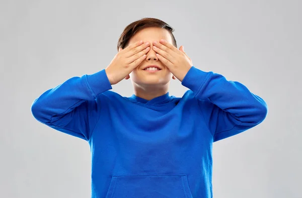 Мальчик в синей толстовке закрывает глаза руками — стоковое фото