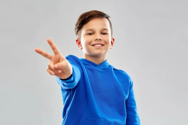 평화 제스처를 보여주는 파란색 후드에 웃는 소년 — 스톡 사진