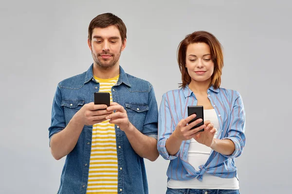 Feliz pareja usando teléfonos inteligentes sobre gris —  Fotos de Stock