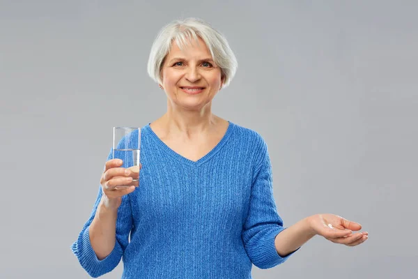 Пожилая женщина со стаканом воды и таблетками — стоковое фото