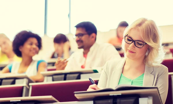 Student tjej skriver till anteckningsboken i föreläsningssalen — Stockfoto