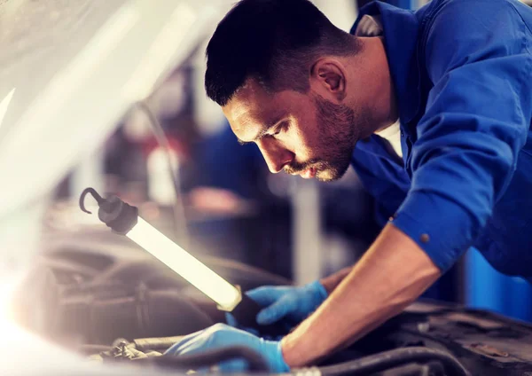 Mecânico homem com lâmpada reparando carro na oficina — Fotografia de Stock