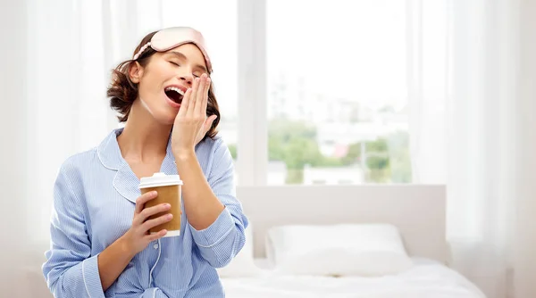 Woman in pajama and eye mask with coffee yawning — Stock Photo, Image