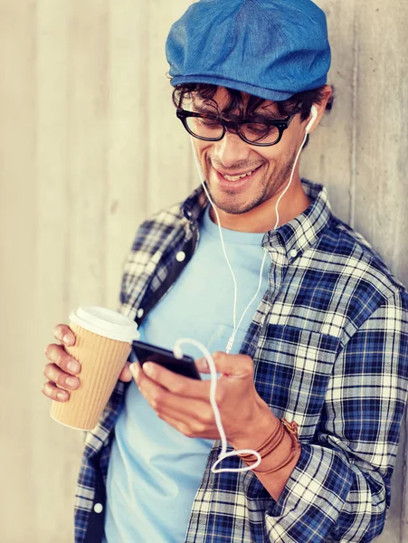 イヤホンとコーヒーを飲みながらスマート フォンを持つ男 — ストック写真