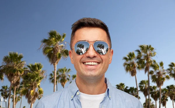 Лицо улыбающегося человека в солнечных очках над пальмами — стоковое фото