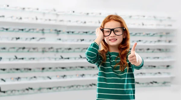 Chica estudiante pelirroja en gafas en la tienda de óptica — Foto de Stock