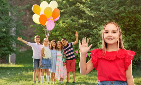 Usměvavá dívka mávající ruku na narozeninovou oslavu v parku — Stock fotografie