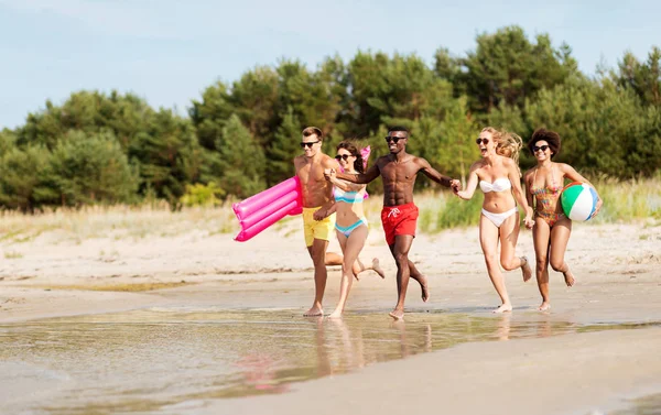 Друзья бегают с пляжным мячом и плавательным матрасом — стоковое фото