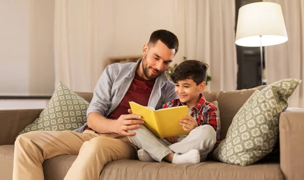 Pai feliz e filho ler sofá livro em casa — Fotografia de Stock
