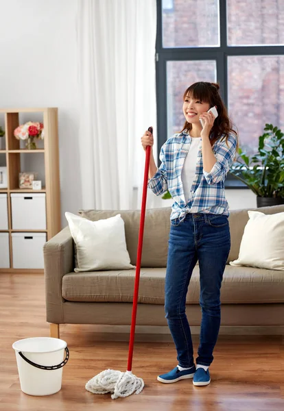 Aziatische vrouw met smartphone dweil vloer thuis — Stockfoto