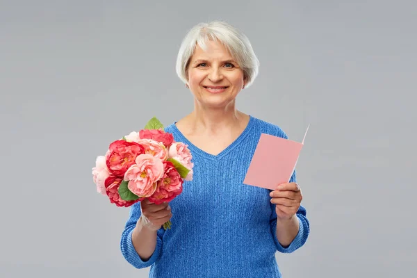 Mulher sênior feliz com flores e cartão de saudação — Fotografia de Stock