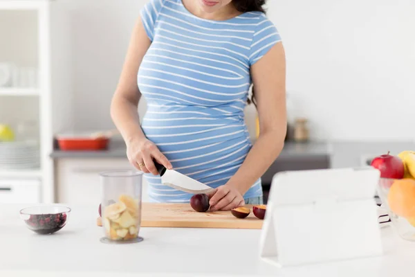 Mujer embarazada picando ciruelas en la cocina casera — Foto de Stock