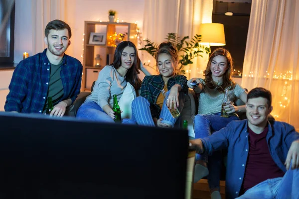 Счастливые друзья с напитками, смотрящие телевизор дома — стоковое фото