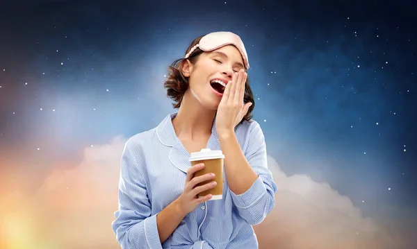 Woman in pajama and eye mask with coffee yawning — Stock Photo, Image
