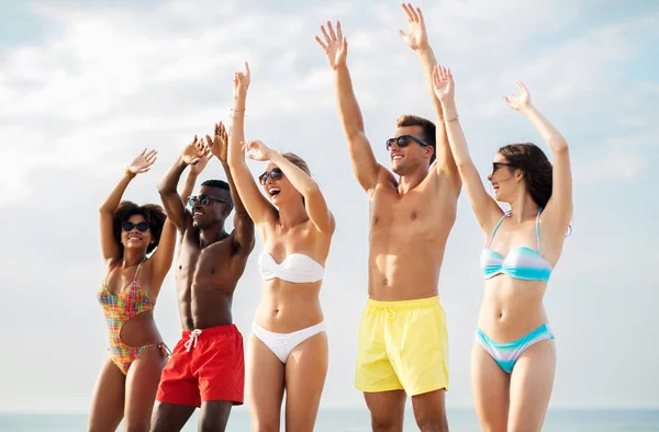Glada vänner med händerna uppe på sommar stranden — Stockfoto